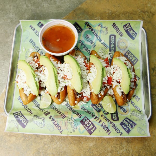 El Vagoncito Chilango's Mexican hot dogs topped with avocado, cheese, and lime, with a side of sauce.