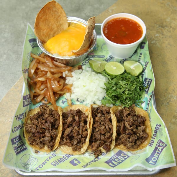 Four El Vagoncito Chilango tacos with sides of onions, cilantro, limes, queso, and consommé.