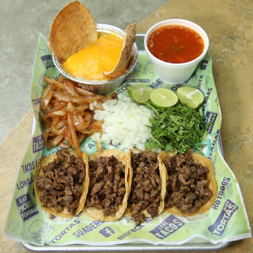Four El Vagoncito Chilango tacos with sides of onions, cilantro, limes, queso, and consommé.