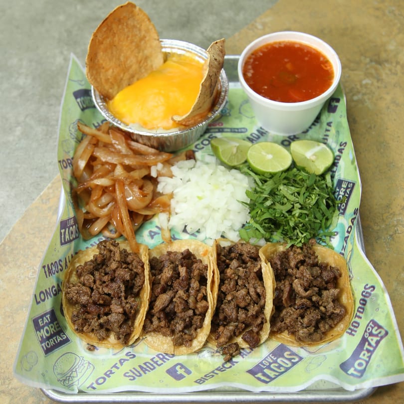 Four El Vagoncito Chilango tacos with sides of onions, cilantro, limes, cheese dip, and consommé.