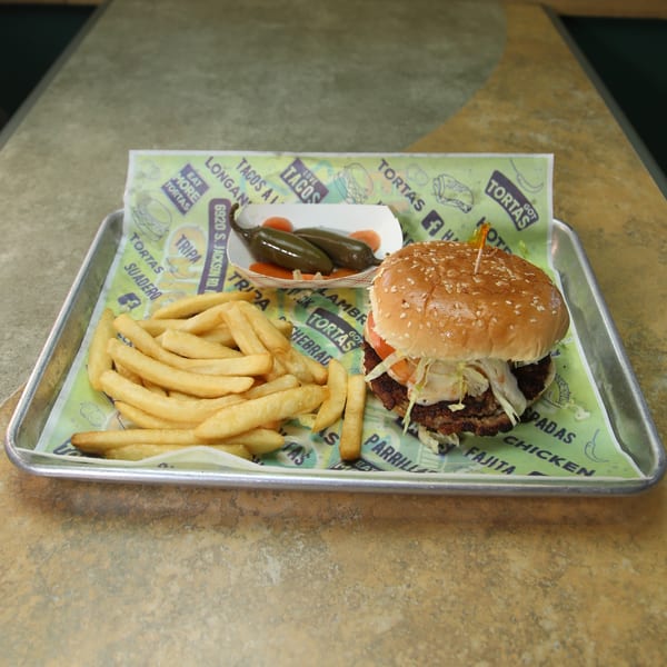 A Mexican burger with fries and pickled jalapeños on a tray with branded paper.