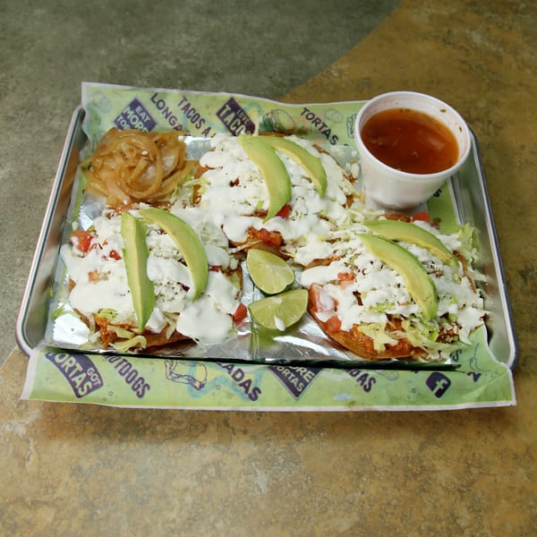 Three El Vagoncito Chilango sopes with avocado, cheese, and crema, served with onions and salsa.