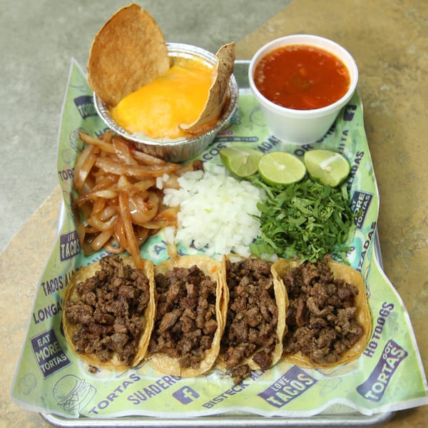 Four El Vagoncito Chilango tacos with sides of cheese dip, broth, onions, cilantro, and limes.