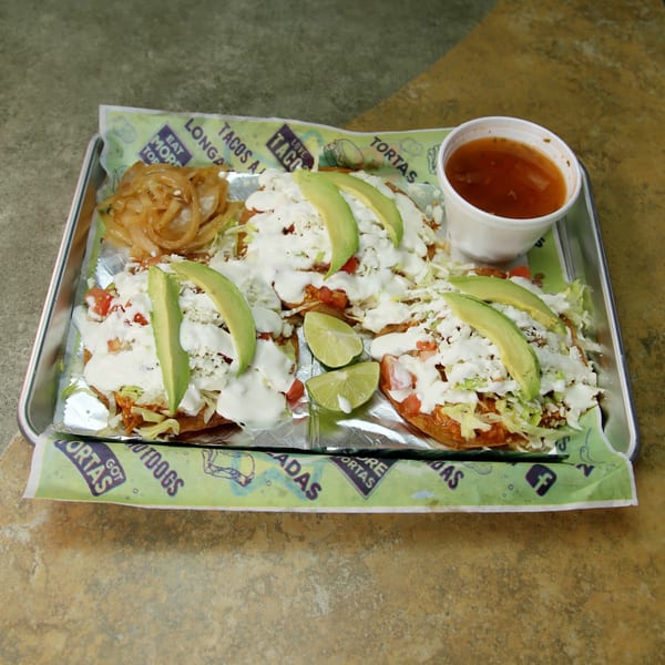 Three Mexican sopes with avocado, cheese, and sour cream, served with onions and salsa.