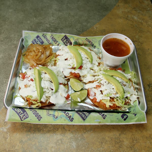 Three Mexican sopes topped with avocado, sour cream, cheese, and lettuce, served with a side of sauce.